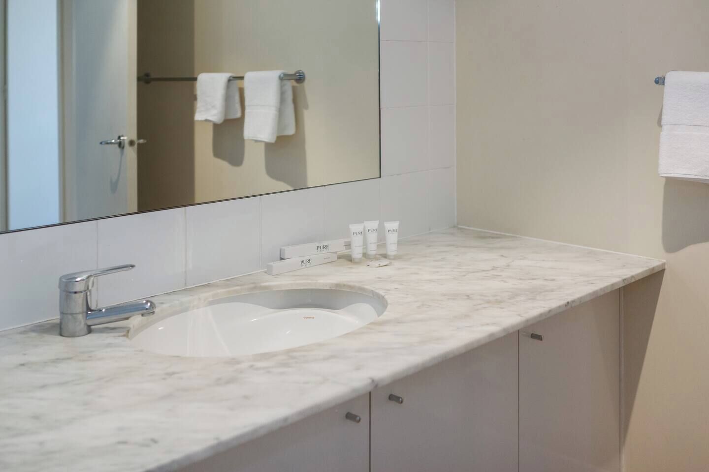 A bathroom with a marble sink, a large mirror, and a towel rack.