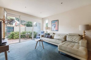 A living room with a beige sofa, a coffee table, and a TV stand. - Patio Charm in Buzzing Richmond with Parking (Richmond)