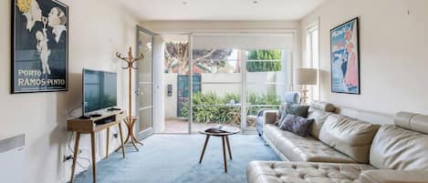 A living room with a leather sofa, a television, a coffee table, and a sliding glass door leading to a balcony.