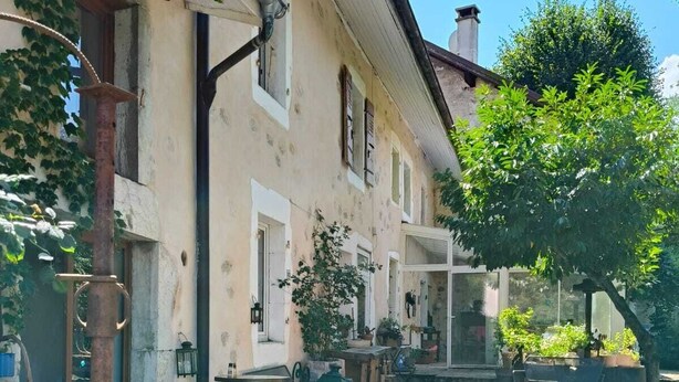 A courtyard with a rustic building, outdoor seating, and a wooden fence.