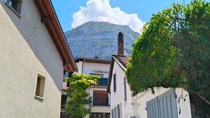 A narrow street with buildings on either side, a tree in the foreground, and a mountain in the background.