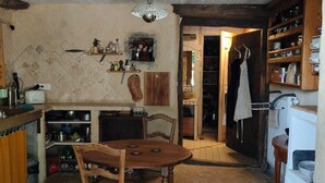 A rustic kitchen with a wooden table, shelves with kitchenware, and a hanging light fixture.