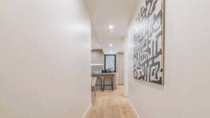 Um corredor com piso de madeira que leva a uma cozinha com eletrodomésticos modernos e banquetas.