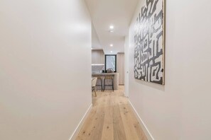 A hallway with wooden flooring leading to a kitchen area with modern appliances and bar stools. - Alexandra Elegance Riverside Living in Style (South Yarra)