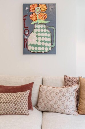A room with a beige sofa, patterned pillows, and a wall-mounted artwork depicting a flower vase. - Alexandra Elegance Riverside Living in Style (South Yarra)