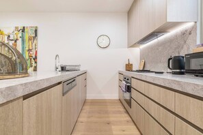 A modern kitchen with wooden cabinets, a dishwasher, a microwave, and a kettle. - Alexandra Elegance Riverside Living in Style (South Yarra)