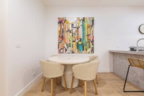 A dining area with a round table and four chairs, a kitchen counter with a sink, and a wall-mounted clock. - Alexandra Elegance Riverside Living in Style (South Yarra)
