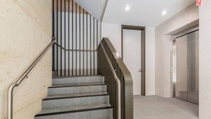Uma escadaria com corrimãos de metal, uma porta e um elevador em um edifício moderno.