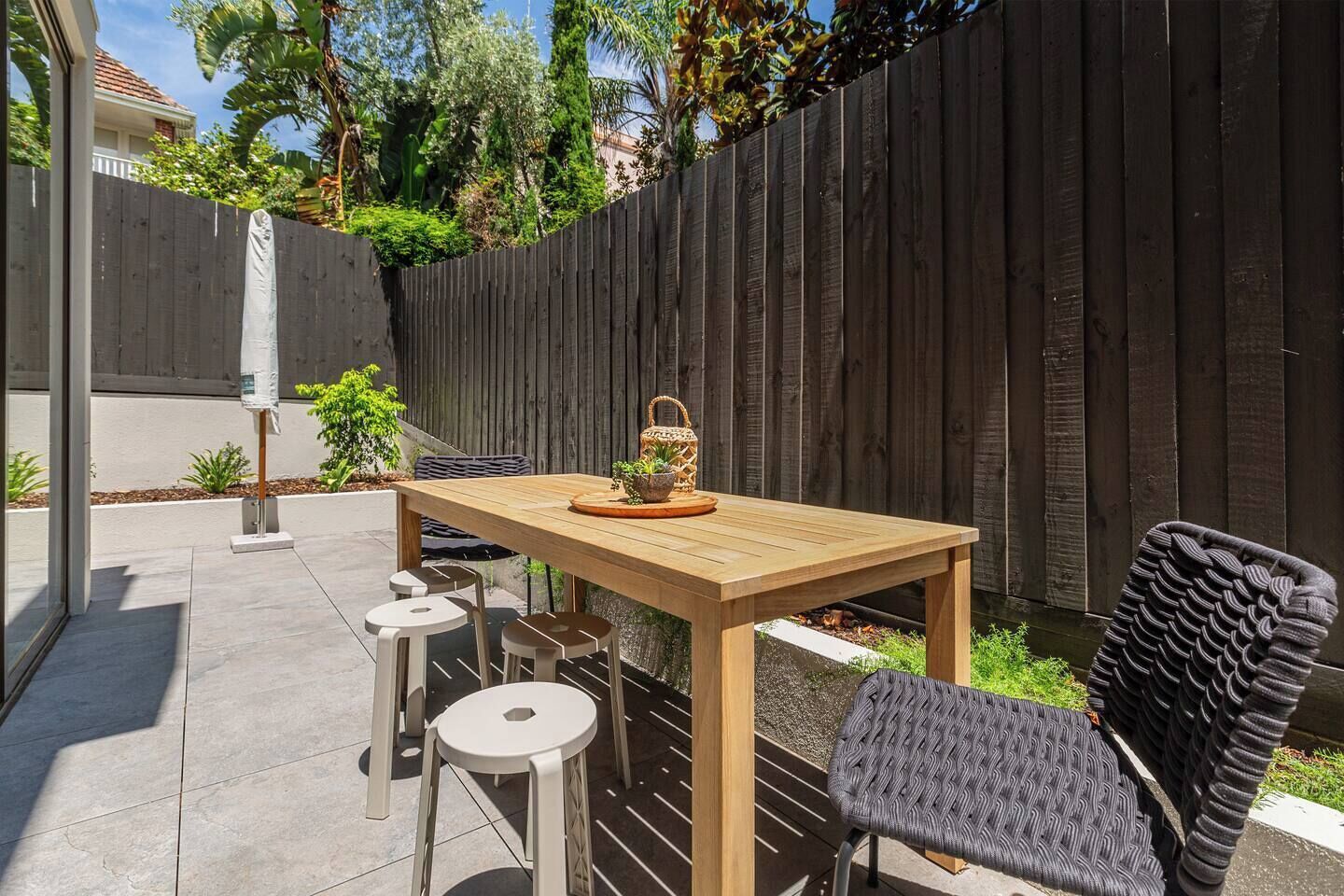 Un patio al aire libre con una mesa de madera y cuatro sillas, rodeado de una valla de madera y vegetación.