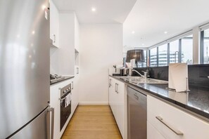 A modern kitchen with stainless steel appliances, a wooden floor, and a view of the city through large windows. - Bay Street Terrace Spacious Indoor Outdoor Design (Port Melbourne)