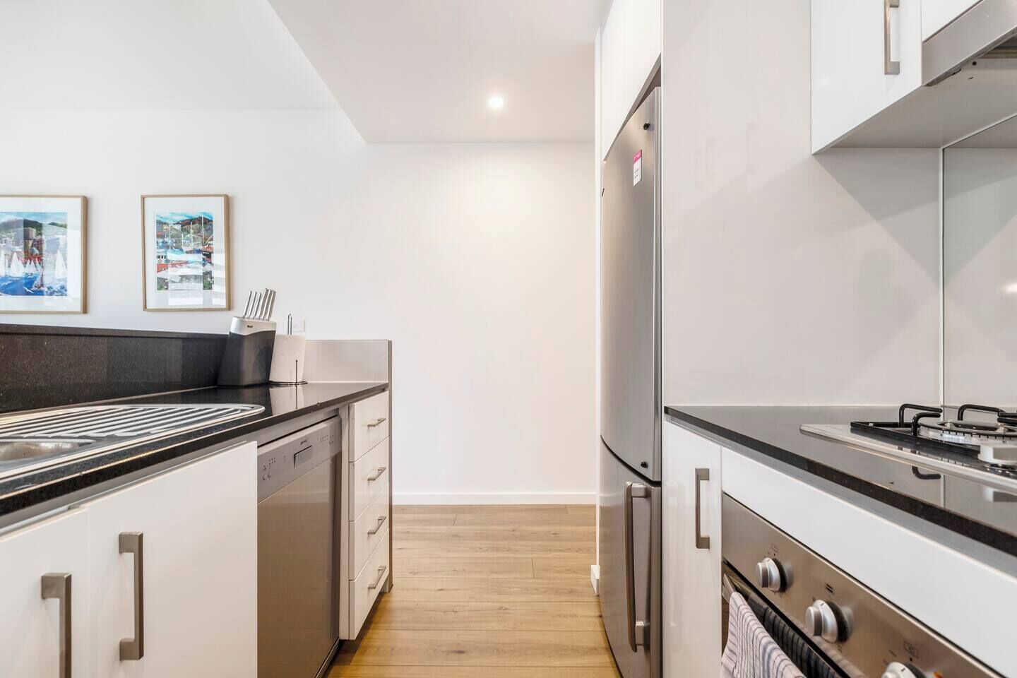 A modern kitchen with stainless steel appliances, white cabinetry, and a wooden floor.