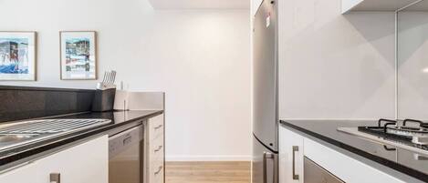 A modern kitchen with stainless steel appliances, white cabinetry, and a wooden floor.