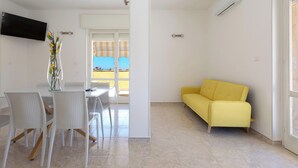 Ein moderner Wohnraum mit Essbereich, einem gelben Sofa und einem an der Wand befestigten Fernseher.