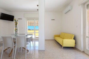 A modern living space with a dining area, a yellow sofa, and a TV mounted on the wall. - Attico Ilary by BarbarHouse (Gallipoli)