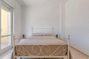A single bed with a metal frame and decorative headboard, positioned against a plain wall with a window on the left. - Attico Ilary by BarbarHouse (Gallipoli)