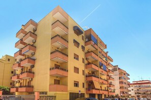 Un immeuble résidentiel à plusieurs étages, doté de balcons et de climatiseurs, avec un ciel bleu dégagé.