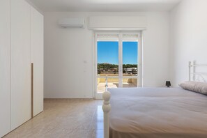 Ein Schlafzimmer mit Bett, Kleiderschrank, Klimaanlage und Blick auf einen Balkon mit Geländer.