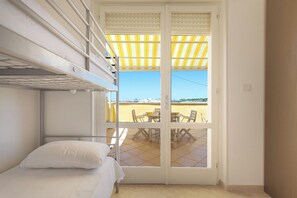Une chambre avec un lit superposé, une petite table avec des chaises et une vue sur une terrasse extérieure, accessible par une porte vitrée.