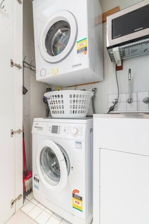 Uma lavanderia com duas máquinas de lavar empilhadas, um micro-ondas em cima e uma cesta na máquina superior.
