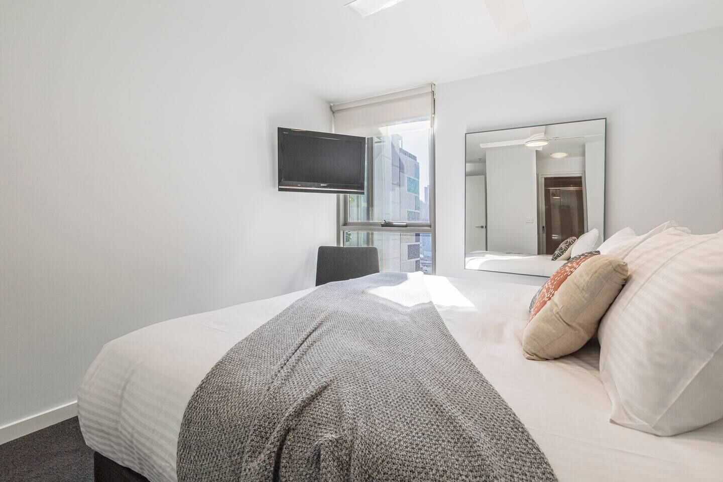 Een moderne hotelkamer met een groot bed, een aan de muur bevestigde televisie, een spiegel en uitzicht op de stad.