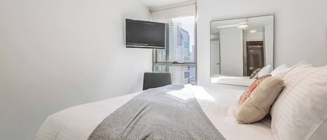 Et moderne hotelværelse med en stor seng, et fjernsyn ophængt på væggen, et spejl og udsigt over byen fra vinduet.