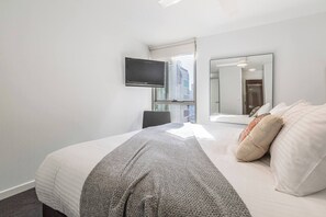 Una moderna camera d'hotel con un grande letto, una TV a parete, uno specchio e vista sulla città dalla finestra.