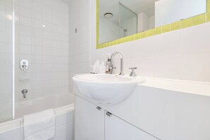 Et moderne badeværelse med en hvid vask, et spejl med guldfarvet ramme og en bruseniche.