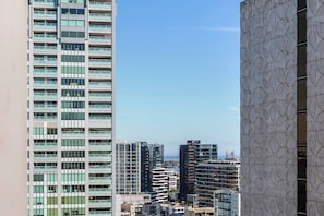 Een hoog gebouw met meerdere verdiepingen en balkons, omringd door andere hoge gebouwen en een heldere lucht.