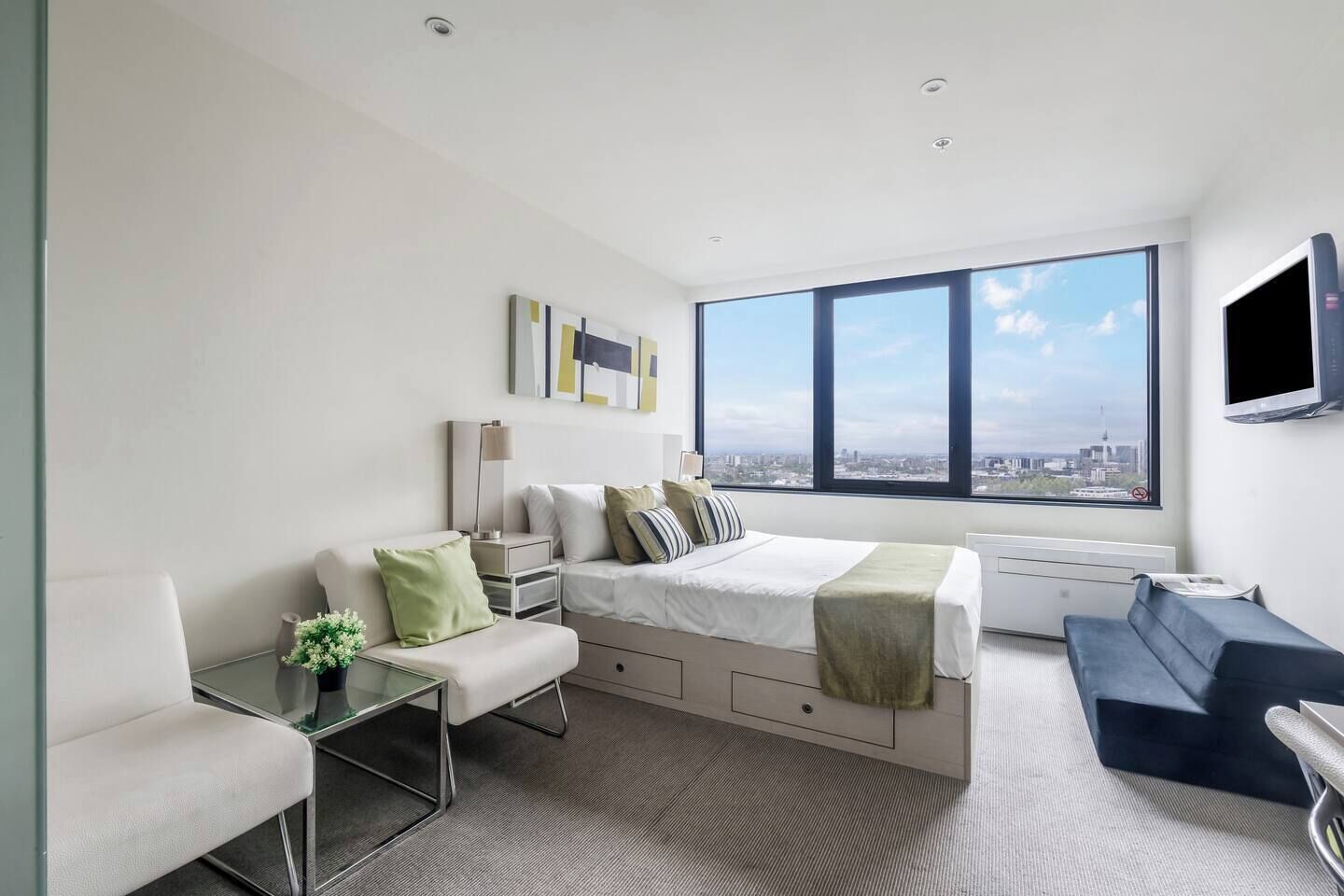 A modern bedroom with a large window, a bed, a desk, and a seating area.
