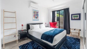 Un dormitorio moderno con una cama, una silla roja, una escalera de madera y una ventana con cortinas.