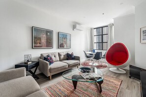 A modern living room with a sofa, a glass coffee table, a red chair, and two framed artworks on the wall. - The New York Edit CBD Living with Private Rooftop (Melbourne)