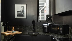 Una cocina moderna con encimera negra, cafetera, microondas y lavabo.
