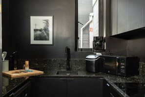 A modern kitchen with a black countertop, a coffee machine, a microwave, and a sink. - The New York Edit CBD Living with Private Rooftop (Melbourne)