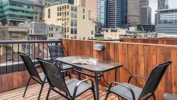 Terraza en la azotea con mesa y sillas, con vistas a un paisaje urbano de edificios modernos.