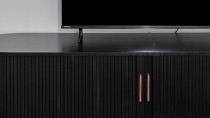Un televisor de pantalla plana montado en la pared sobre un mueble negro con líneas verticales y dos tiradores.