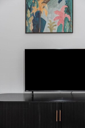 A flat-screen TV mounted on a wall above a black cabinet with vertical lines and two handles. - The New York Edit CBD Living with Private Rooftop (Melbourne)