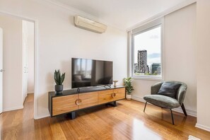 Ein modernes Wohnzimmer mit Flachbildfernseher, Holzschrank und grauem Sessel.