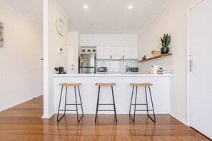Eine moderne Küche mit weißen Schränken, einem Edelstahl-Kühlschrank und drei Holzbarhocker.