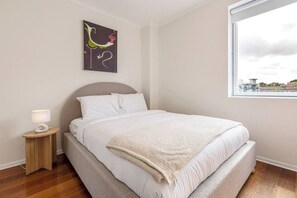 A bedroom with a bed, a nightstand, a lamp, a window with a view, and a wall art piece. - Cityscape Retreat Modern Comfort near Yarra River (Southbank)
