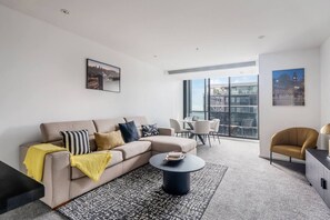 A modern living room with a sofa, coffee table, and a dining area with chairs. - Grandview 40 Steps to the Yarra w Pool and Parking (Southbank)