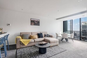 A modern living room with a sofa, coffee table, and chairs. There is a balcony with a view. - Grandview 40 Steps to the Yarra w Pool and Parking (Southbank)