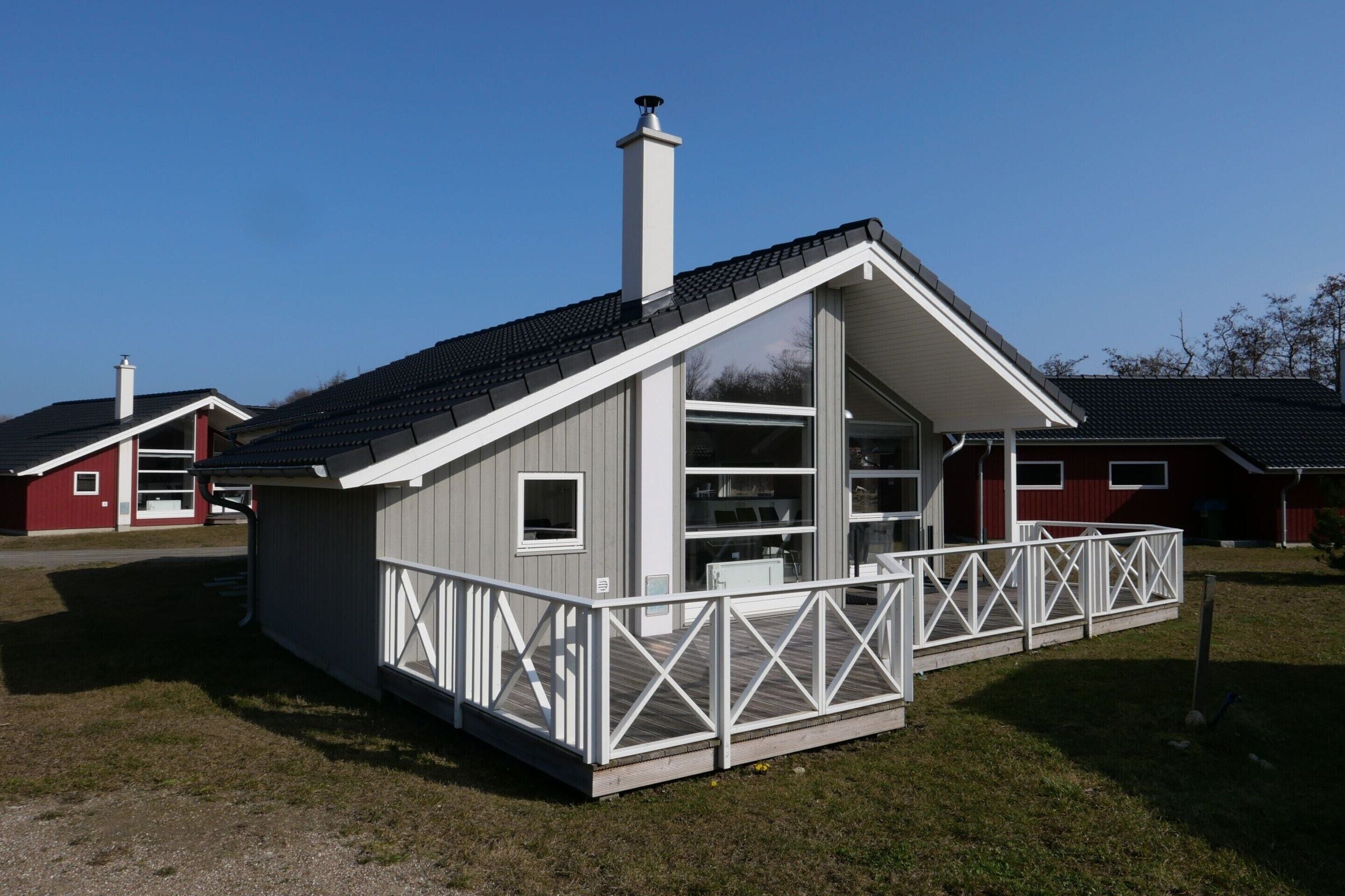 A small, single-story cabin with a sloped roof, a balcony with a white railing, and a chimney.