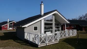 A small, single-story cabin with a sloped roof, a balcony with a white railing, and a chimney.