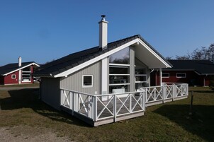 A small, single-story cabin with a sloped roof, a balcony with a white railing, and a chimney.