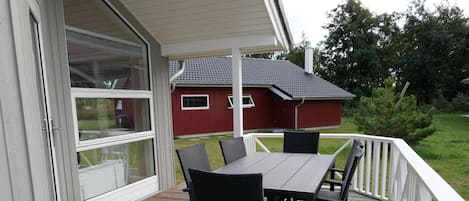 A covered outdoor deck with a table and chairs, a red barn in the background, and a white railing.