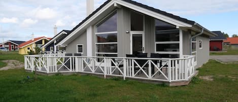 A single-story house with a white exterior, large windows, and a covered porch with chairs.