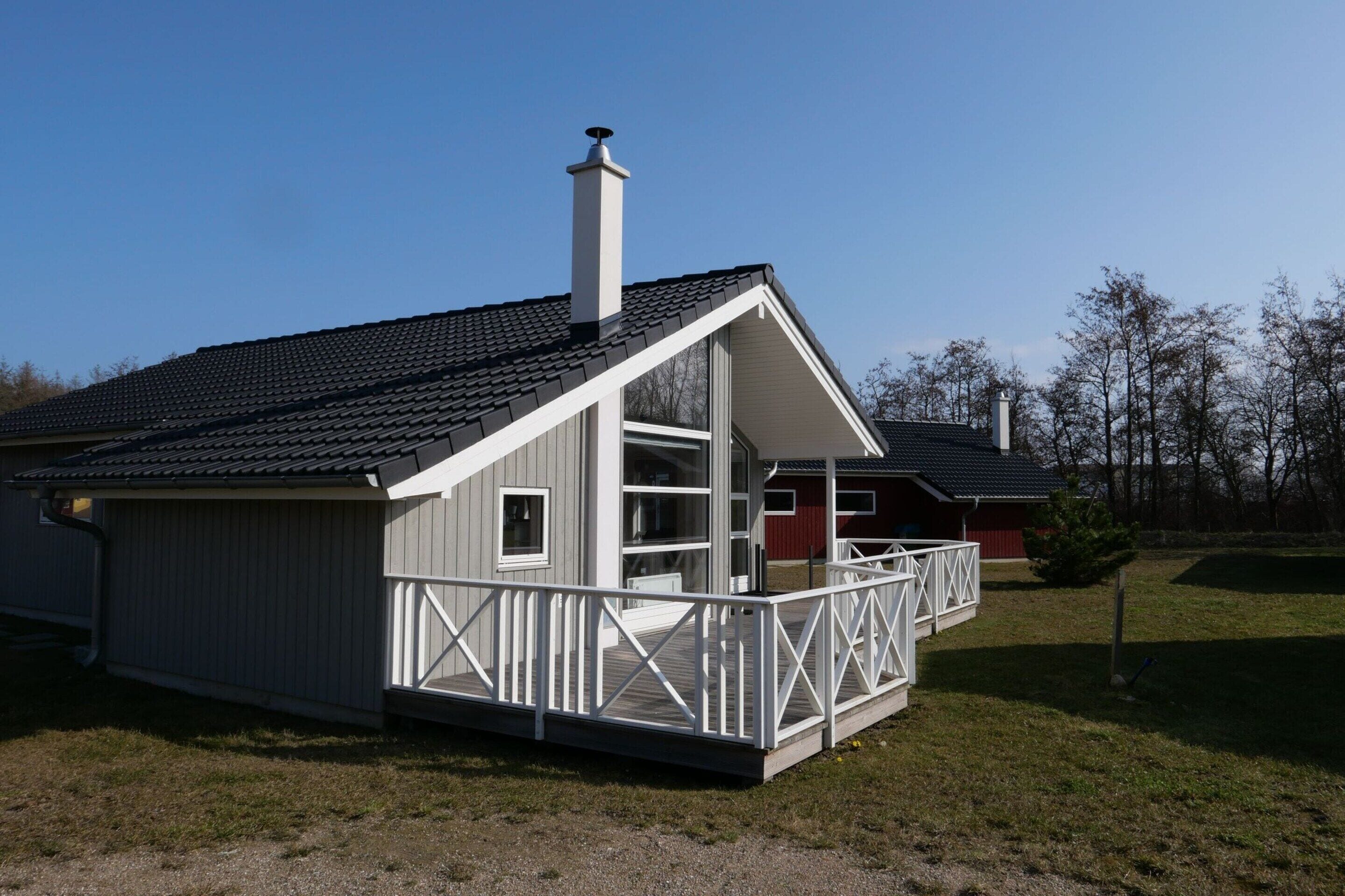 A single-story house with a balcony, a chimney, and a red barn in the background.