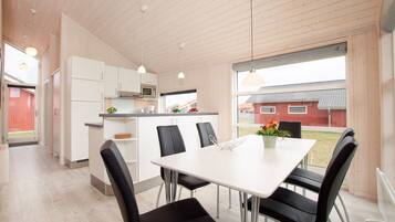 A modern kitchen with white cabinets, a microwave, and a dining area with a white table and black chairs.
