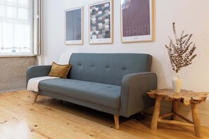 Um quarto com um sofá cinzento, uma mesa lateral de madeira com um vaso, e três obras de arte emolduradas na parede.
