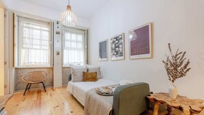 A cozy bedroom with a bed, a chair, a small table, and a hanging light fixture. - Historic Se Apartment Prime Location by HostWise (Sé)